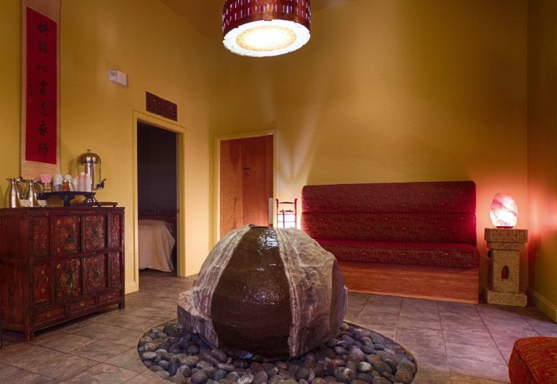 A large circular rock fountain in the center of the waiting area at Earthling Day Spa in Charleston SC. Pretty lighting and benches surround the fountain.