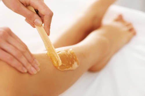 A esthetician applies sugar paste to the legs using a wooden stick during a body sugaring service.